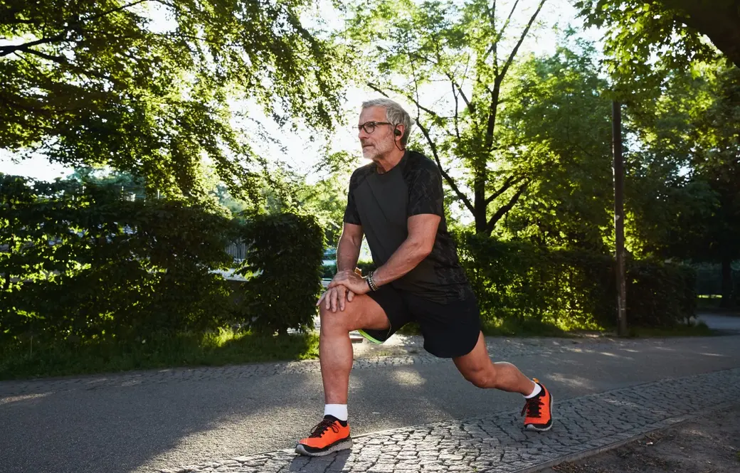 Мъж със спортно облекло, който се разтяга в парк