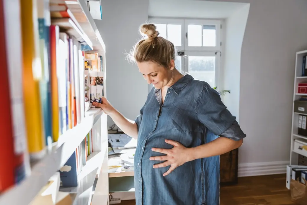 Бременна жена, която избира книга от библиотека у дома