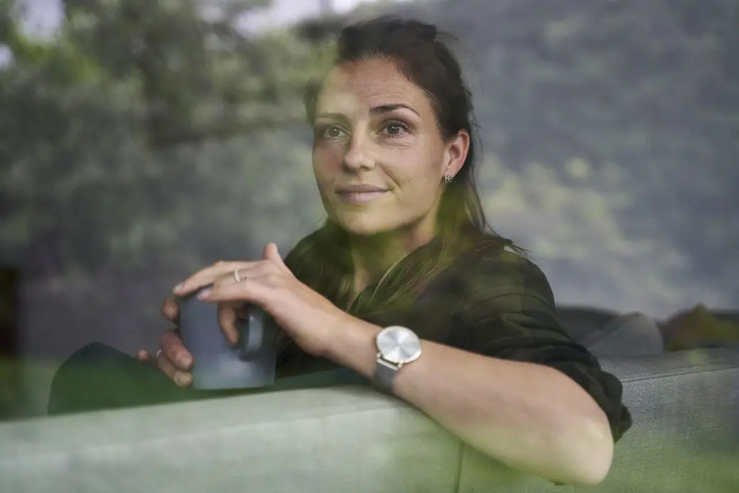 Жена, която гледа през прозорец и държи чаша за кафе