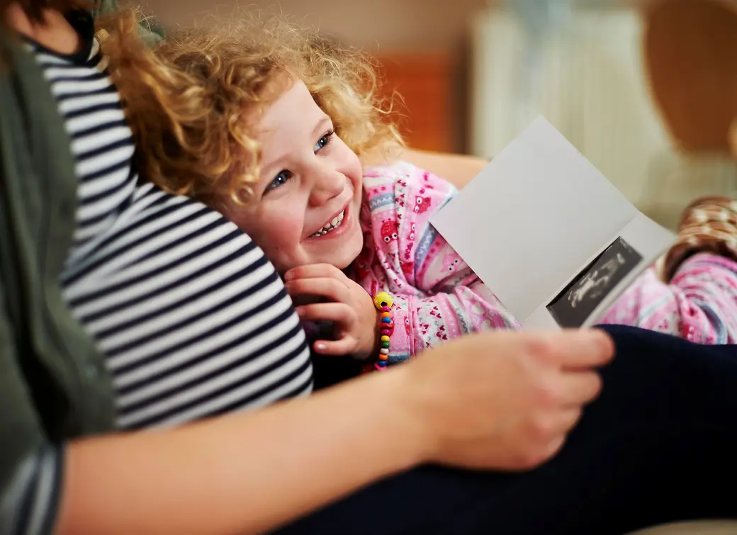 Бременна жена прегръща дъщеря си и гледат снимка от ехограф