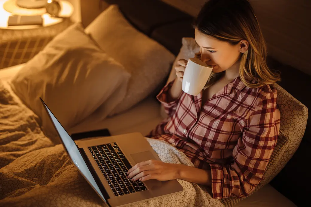 Жена, която чете на лаптоп в леглото и пие чай