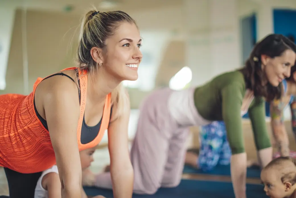 Бременна жена, която прави йога на постелка в салон с други жени