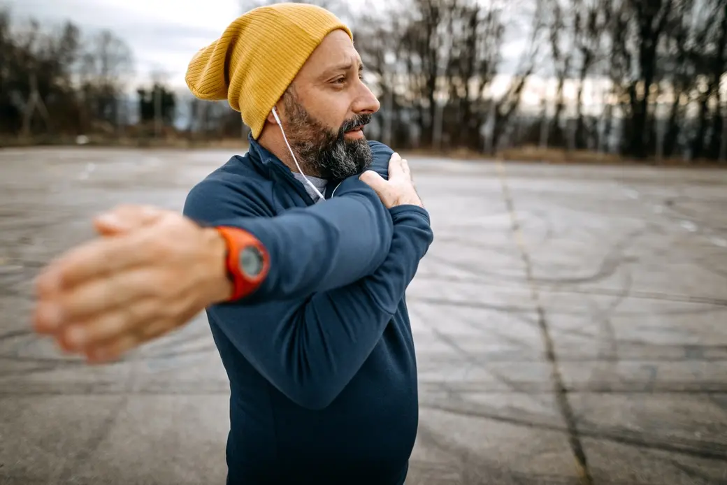 Мъж със спортно облекло, който се разтяга в парк